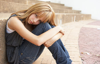 unhappy female teenage student sitting outside on college steps